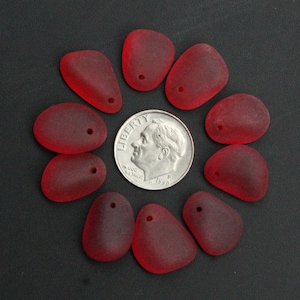 May include: Ten red glass sea glass beads with a hole drilled through each bead. The beads are arranged in a circle around a US dime.
