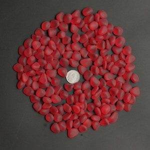 May include: A large quantity of small, red glass pebbles. The pebbles are smooth and translucent, and they are arranged in a circular pattern.