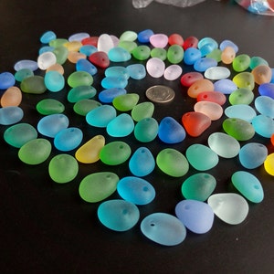 May include: Assortment of colorful, frosted glass beads in various shades of blue, green, red, and yellow. The beads are oval shaped and have a hole drilled through the top for stringing.