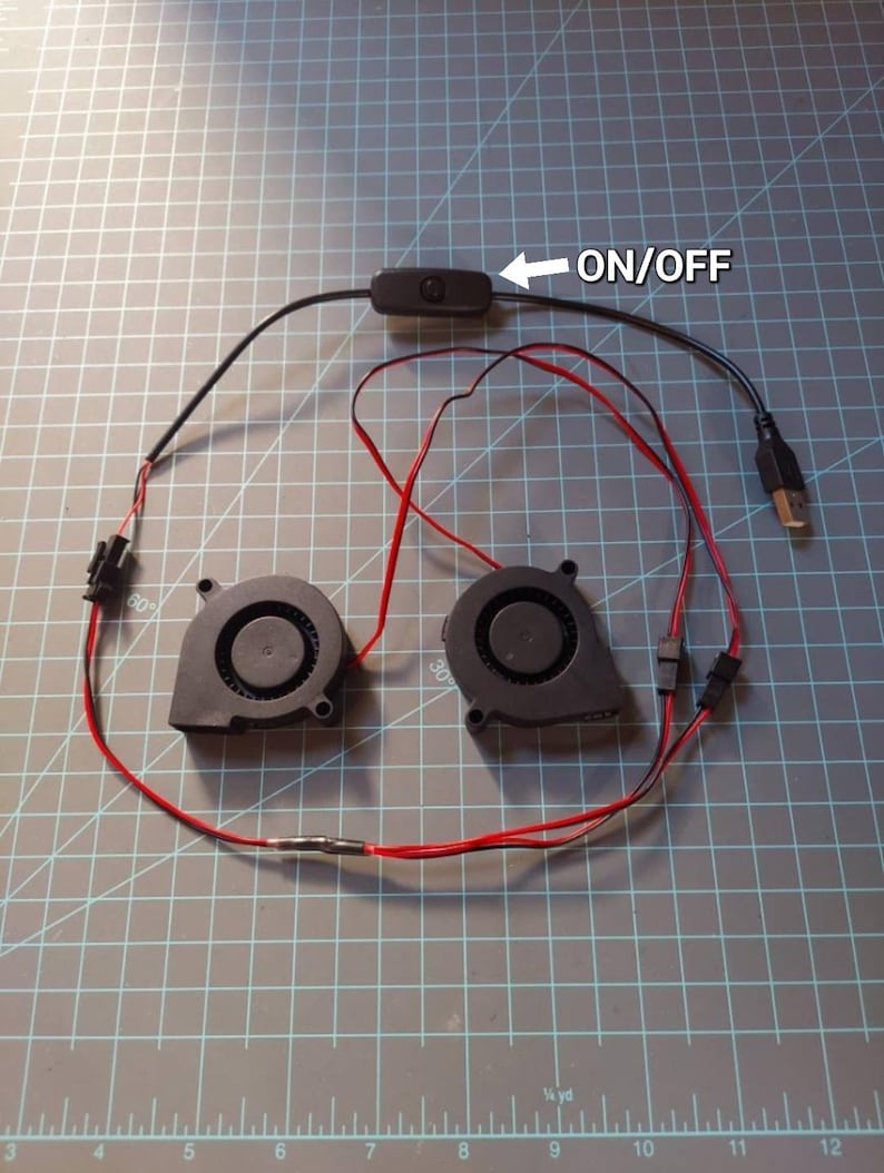 May include: An overhead shot shows two small black fans connected by red and black wires. A black on/off switch is connected to the fans. A USB connector is visible. The text "ON/OFF" is next to the switch.