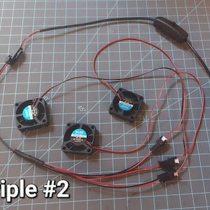 May include: A set of three small black fans with blue and white labels, connected by red and black wires. The wires lead to a USB connector and a switch. The text "Triple #2" is visible.