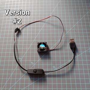 May include: A small black fan with blue blades, connected to a USB plug and a black on/off switch. Red and black wires are visible. The text "Version #2" is in the upper left corner.