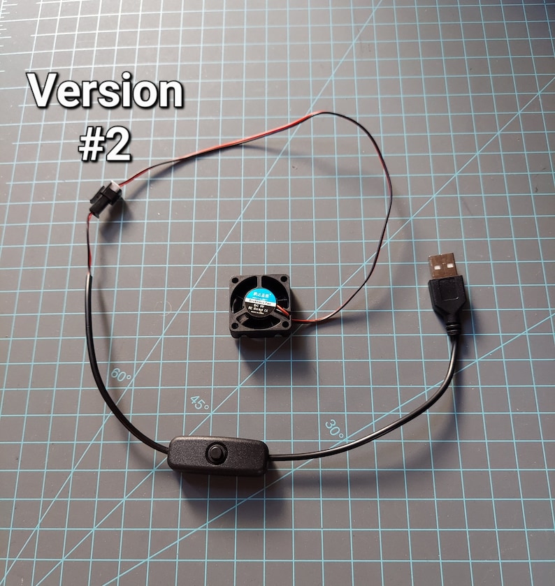 May include: A small black fan with blue blades, connected to a USB plug and a black on/off switch. Red and black wires are visible. The text "Version #2" is in the upper left corner.