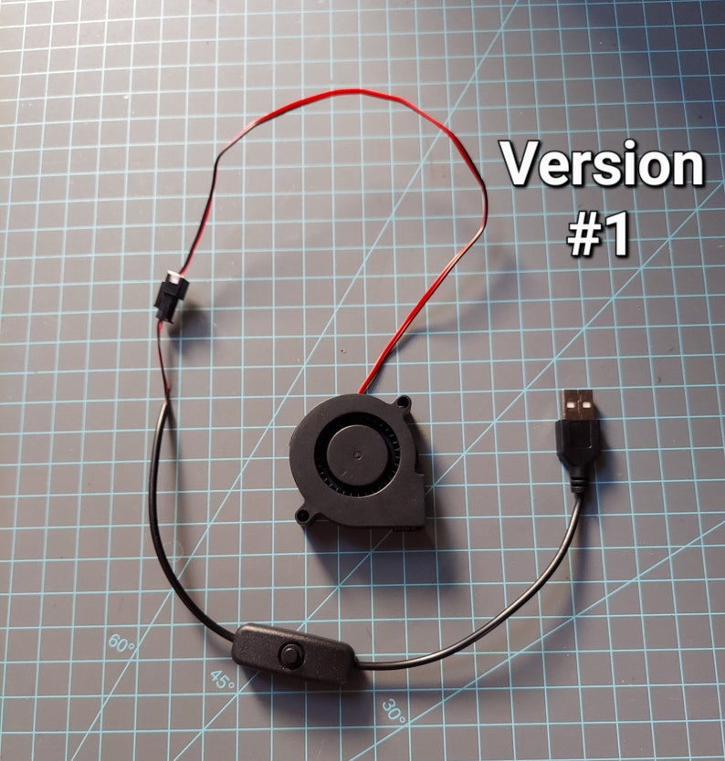 May include: A black USB-powered fan with a red and black wire, a black on/off switch, and the text "Version #1". The fan is circular with a central intake and a USB connector.