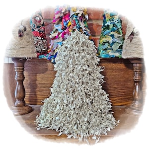 May include: A collection of decorative Christmas trees and lamp shades. The central tree is a light beige color, made of small, leaf-like elements. Other trees are made of colorful fabric scraps. The lamp shades are wrapped in twine.