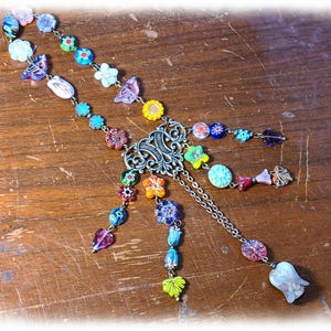 May include: A colorful necklace with floral and abstract glass beads. The necklace features a silver-toned filigree centerpiece and delicate chain accents. The beads are in various shapes and colors, including flowers, leaves, and teardrops.