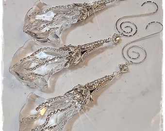 May include: Three clear, faceted crystal ornaments shaped like bell-like flowers. Each piece features a silver-toned metal cap adorned with small clear rhinestones, a dangling rhinestone chain, and a silver metal spiral hook for hanging purposes.