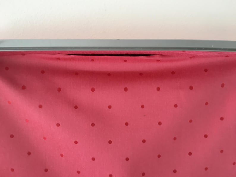 Pu&ograve; includere: Un tessuto rosa vivace caratterizzato da un motivo ripetitivo di piccoli pois rosso scuro. Il tessuto &egrave; drappeggiato e fissato a una cornice metallica grigia, liscia e orizzontale, che corre lungo il bordo superiore dell'immagine.