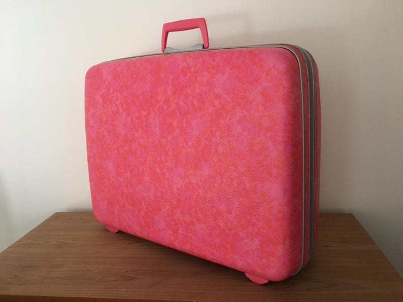 Pu&ograve; includere: Una valigia rigida rettangolare con un vivace motivo maculato rosa e arancione. Il bagaglio include una maniglia superiore rosa a tinta unita, una chiusura a zip color argento e piccoli piedini integrati sulla base.