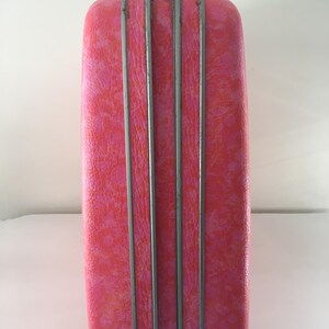 Pu&ograve; includere: Una valigia rigida rettangolare caratterizzata da un vivace motivo maculato rosa e arancione. L'esterno &egrave; diviso da tre strisce decorative verticali in metallo argentato che corrono lungo il centro, con una piccola chiusura metallica in alto.