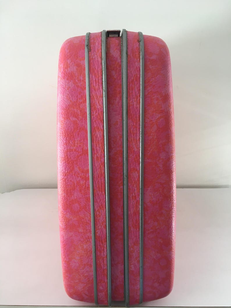 Pu&ograve; includere: Una valigia rigida rettangolare caratterizzata da un vivace motivo maculato rosa e arancione. L'esterno &egrave; diviso da tre strisce decorative verticali in metallo argentato che corrono lungo il centro, con una piccola chiusura metallica in alto.