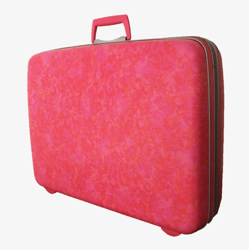 Pu&ograve; includere: Una valigia rigida rettangolare di un vivace colore rosa con una superficie testurizzata e maculata. Il bagaglio presenta una maniglia superiore rosa abbinata e una chiusura a zip color argento lungo tutto il perimetro della valigia.