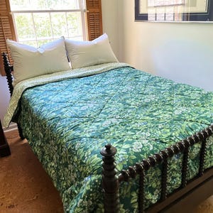May include: A dark brown wooden bed frame with a spindle design features a quilted comforter in a vibrant green floral pattern. Two white pillows rest at the head of the bed, which is positioned in front of a window with wooden shutters.