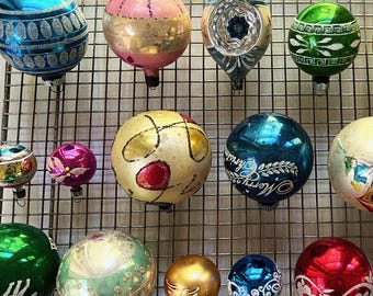 May include: A collection of vintage Christmas ornaments in various shapes and colors. The ornaments include round, teardrop, and starburst designs, with colors like blue, pink, green, gold, and red. Some ornaments have intricate patterns and glitter accents, while others feature the text "Merry Christmas".