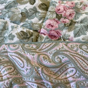May include: A quilted textile featuring two distinct patterns. The top section displays a floral print with pink roses and sage green leaves on a white background. The bottom section shows a paisley pattern in shades of pink, sage green, and cream.