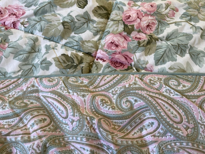 May include: A quilted textile featuring two distinct patterns. The top section displays a floral print with pink roses and sage green leaves on a white background. The bottom section shows a paisley pattern in shades of pink, sage green, and cream.