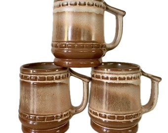 Può includere: Tre tazze in ceramica marrone con una glassa bianca e dettagli marroni. Le tazze hanno un corpo arrotondato e un manico.
