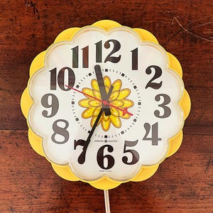 May include: A yellow flower-shaped clock with black numbers and a flower design in the center. The clock face reads "GENERAL ELECTRIC" and "MADE IN U.S.A."