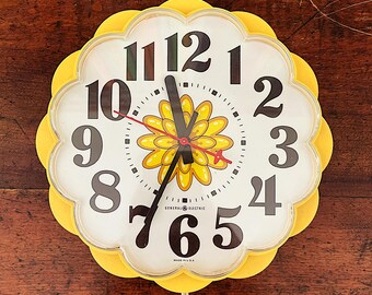 May include: A yellow flower-shaped clock with black numbers and a flower design in the center. The clock face reads "GENERAL ELECTRIC" and "MADE IN U.S.A."