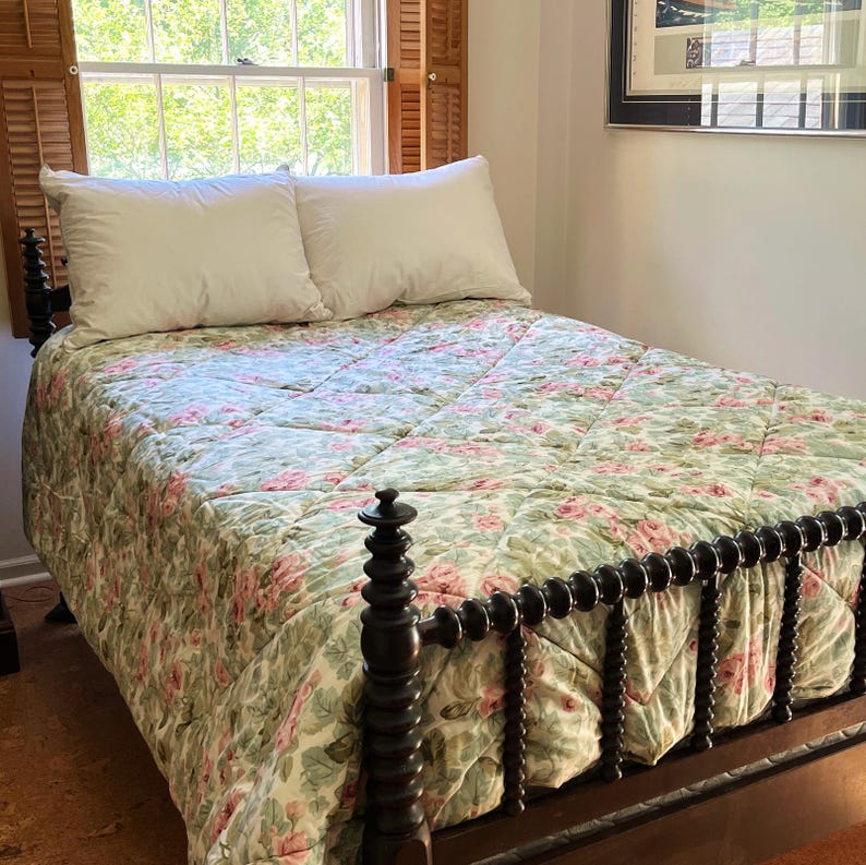 May include: A bed featuring a dark brown wooden frame with a spindle-style headboard and footboard. The bed is dressed in a quilted comforter with a green and pink floral pattern and two plain white pillows positioned against the headboard.