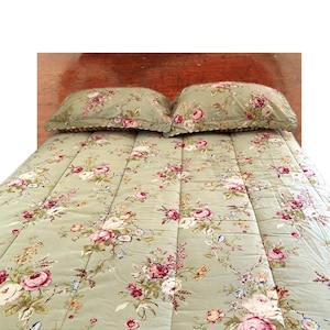 May include: A bed with a floral patterned comforter and two matching pillowcases. The comforter and pillowcases have a light green background with pink, red, and white roses and other flowers. The bed has a wooden headboard.
