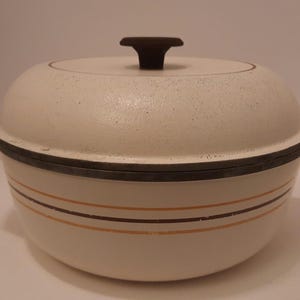 May include: A round, off-white Dutch oven with a speckled finish and a dark brown knob on the lid. The pot features two dark brown horizontal stripes and one orange horizontal stripe encircling the body, with dark brown side handles.