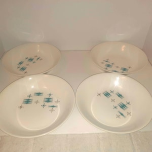 May include: A set of four round, off-white bowls featuring a repeating pattern of teal geometric shapes and small star-like accents. Each bowl has a smooth, curved rim and a shallow basin, with the decorative print positioned off-center.