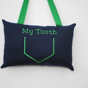 May include: A blue fabric pillow with a green pocket and the text "My Tooth" embroidered on the front. The pillow has green fabric loops for hanging.
