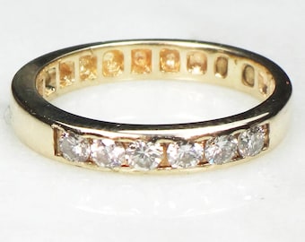 May include: A gold band ring with a row of small, clear diamonds set in a channel setting.