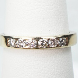 May include: A gold band with a row of small, clear diamonds set in the metal.