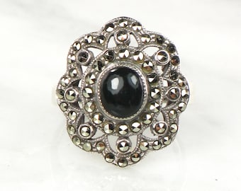 Könnte beinhalten: Ein silberner Ring mit einem schwarzen Edelstein, umgeben von einem floralen Design aus Markasit-Steinen.
