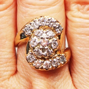 May include: A gold ring with a large cluster of diamonds in the center. The diamonds are set in a swirl pattern and are surrounded by smaller diamonds.