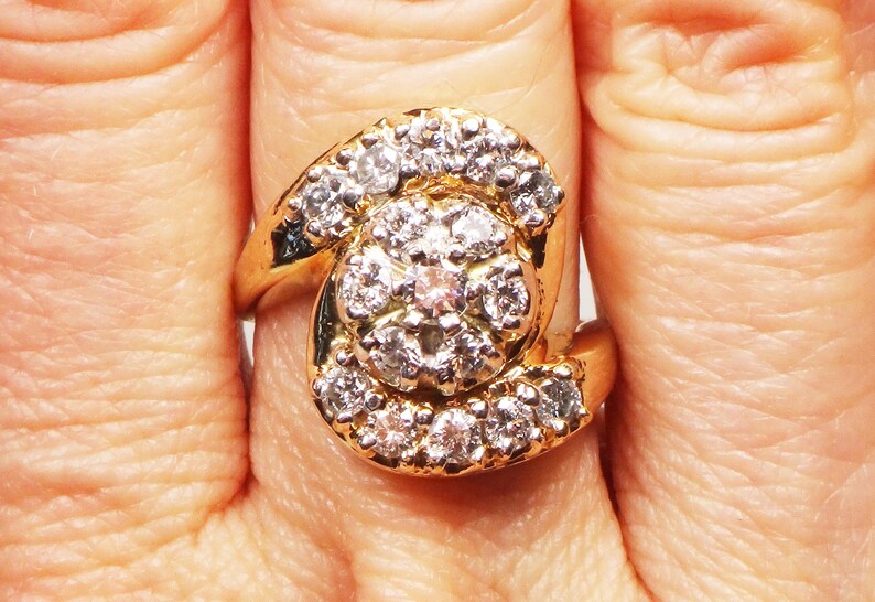 May include: A gold ring with a large cluster of diamonds in the center. The diamonds are set in a swirl pattern and are surrounded by smaller diamonds.