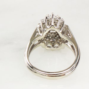 Op de afbeelding: Een zilveren ring met een grote, ronde, veelzijdige steen omringd door kleinere stenen. De ring is gezet in een delicaat, ingewikkeld ontwerp.