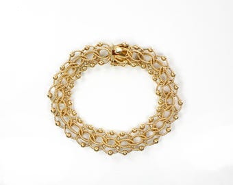 May include: A gold-toned bracelet with a delicate, intricate design. The bracelet is made of linked, twisted wire with small, round beads.