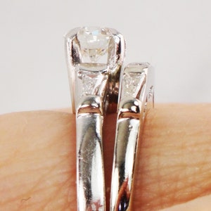 May include: A pair of silver wedding bands with a large, round diamond set in the center of the top band.