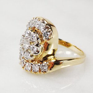 May include: A gold ring with a large cluster of diamonds set in a swirl pattern. The ring is set on a white background.