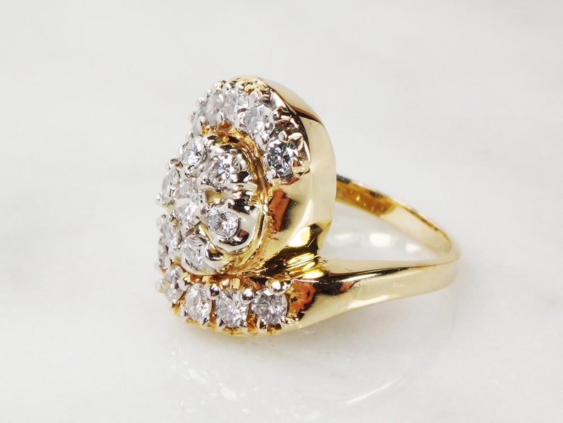May include: A gold ring with a large cluster of diamonds set in a swirl pattern. The ring is set on a white background.