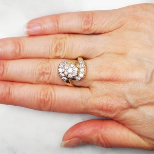 May include: A gold ring with a large, round, center diamond surrounded by smaller diamonds. The ring has a twisted band.