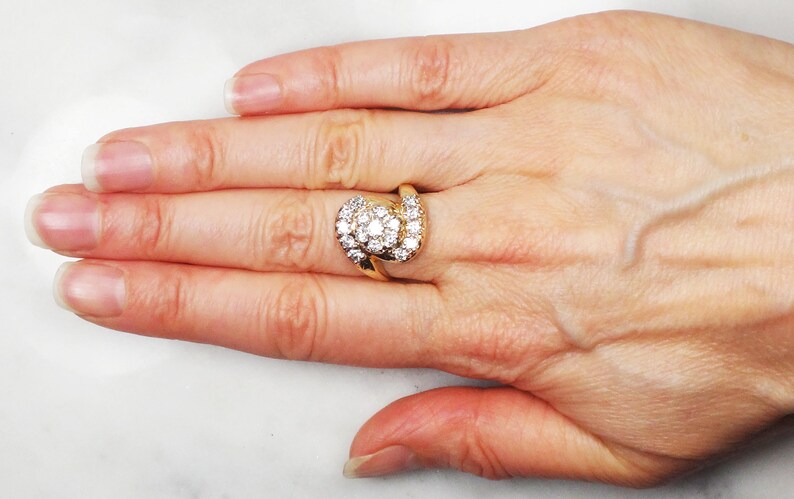 May include: A gold ring with a large, round, center diamond surrounded by smaller diamonds. The ring has a twisted band.