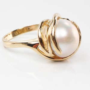 May include: A gold ring with a large, white pearl set in a delicate, swirling design.