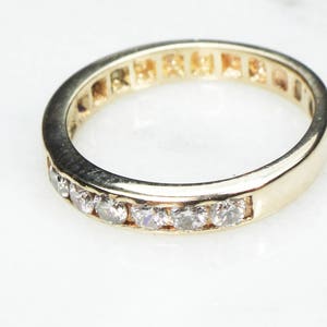 May include: A gold band with a row of small, clear diamonds set into the metal.