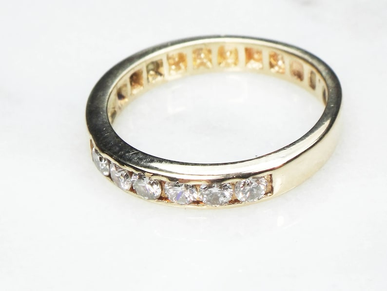 May include: A gold band with a row of small, clear diamonds set into the metal.