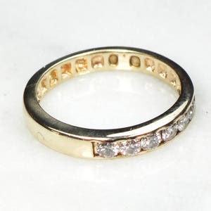 May include: A gold band ring with a row of small, clear diamonds set in the band.
