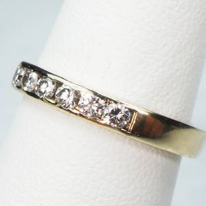 May include: A gold band ring with a row of small, clear diamonds set in the band.