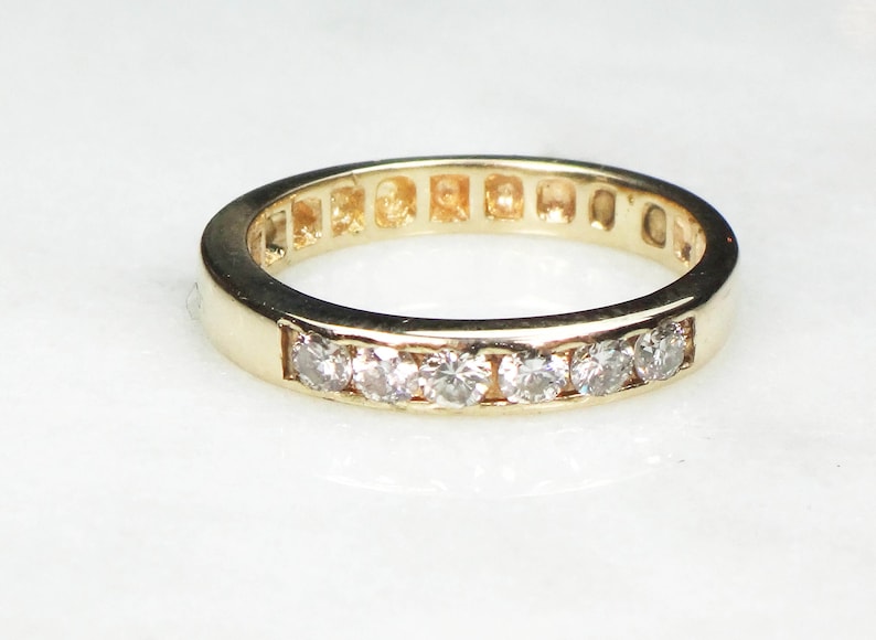 May include: A gold band ring with a row of small, clear diamonds set in a channel setting.
