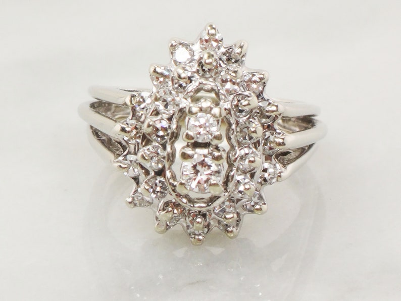 Op de afbeelding: Een zilveren ring met een grote, ovale cluster van diamanten. De ring heeft een delicaat, multiband ontwerp.
