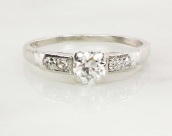 May include: A silver engagement ring with a single round diamond and two smaller diamonds on each side.