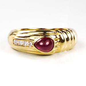 May include: A gold ring with a red gemstone and a row of clear gemstones.
