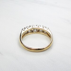 May include: A gold band ring with a row of clear round gemstones set in a prong setting.